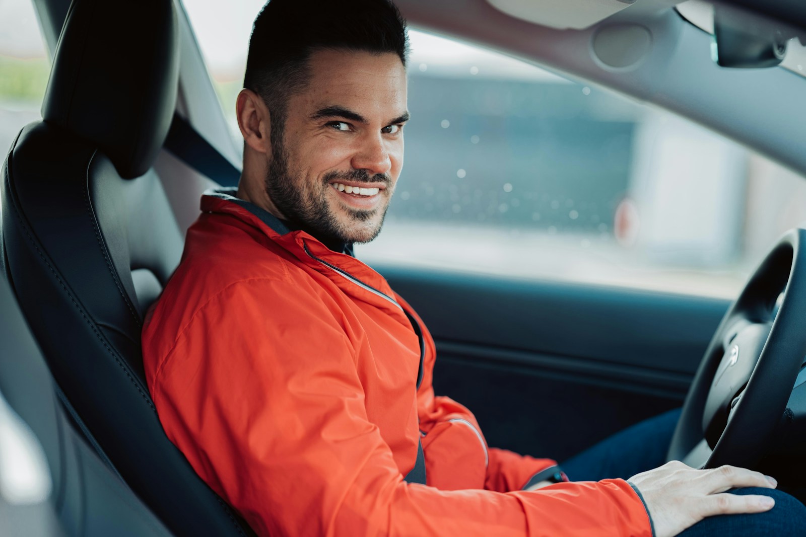 man in orange jacket sitting on car seat